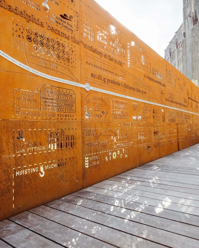 An image of the Story Wall at the Rail Park: an 80 foot galvanized steel wall that illustrates an 1895 atlas of Philadelphia with cutout icons of the businesses that were around the neighborhood at that time