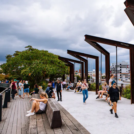 Image of a sunny day on the park near the iconic industrial swings. Lots of visitors can be seen walking, swinging, and seated at the benches.