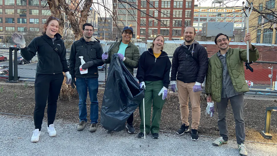 Six volunteers waving and holding a variety of clean-up supplies on the Rail Park