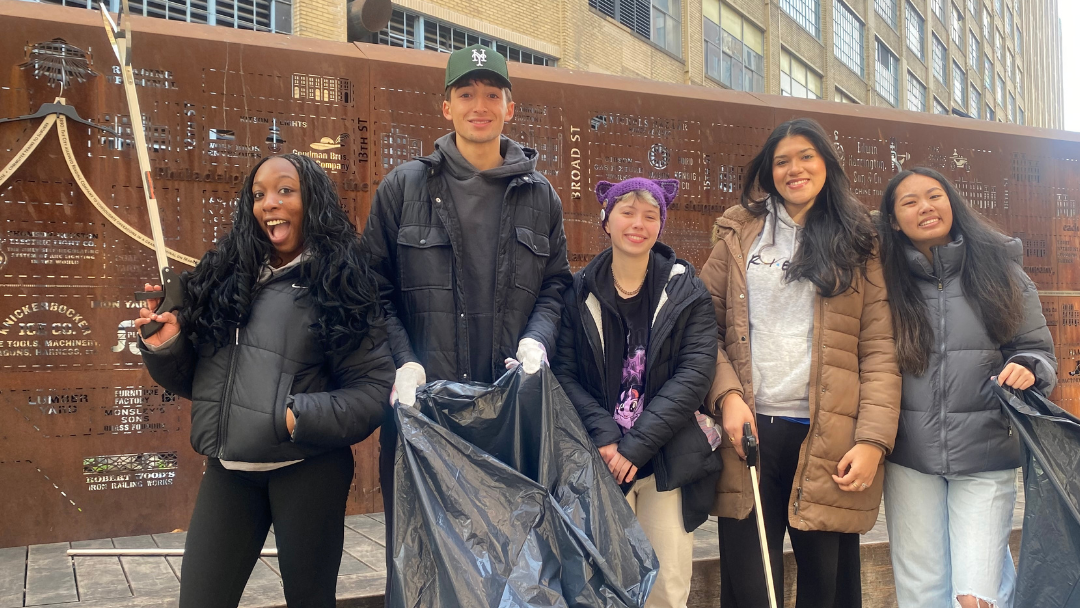 Photo of five smiling students holding trash bags and litter grabbers
