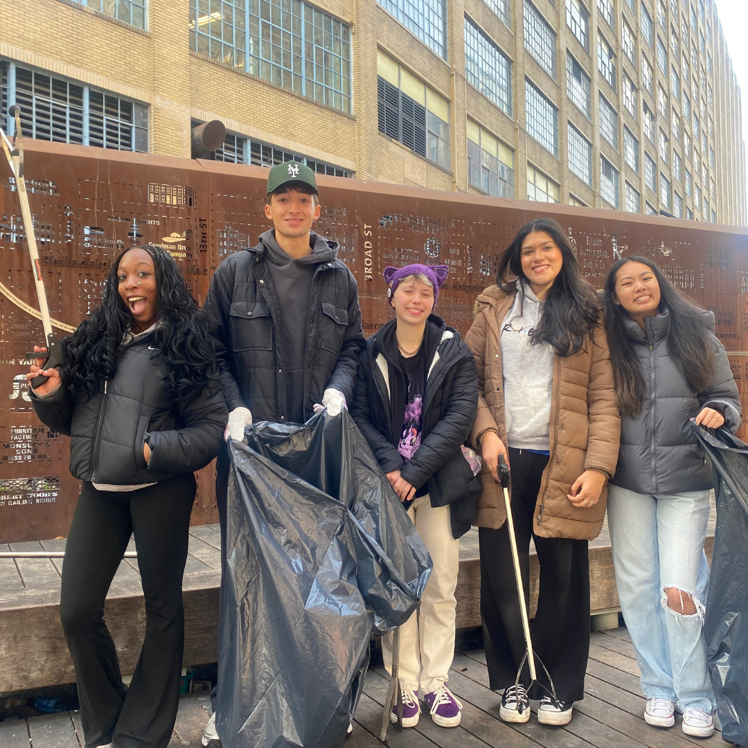 Photo of five smiling students holding trash bags and litter grabbers