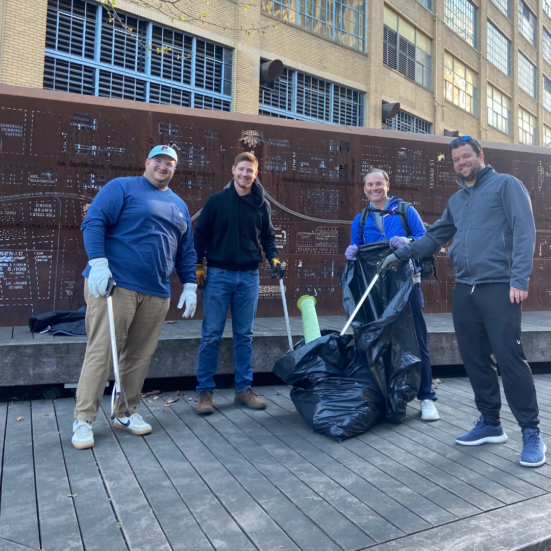 Four male volunteers using trash grabbers to place litter in a garbage bag