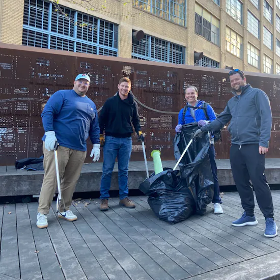 Four male volunteers using trash grabbers to place litter in a garbage bag