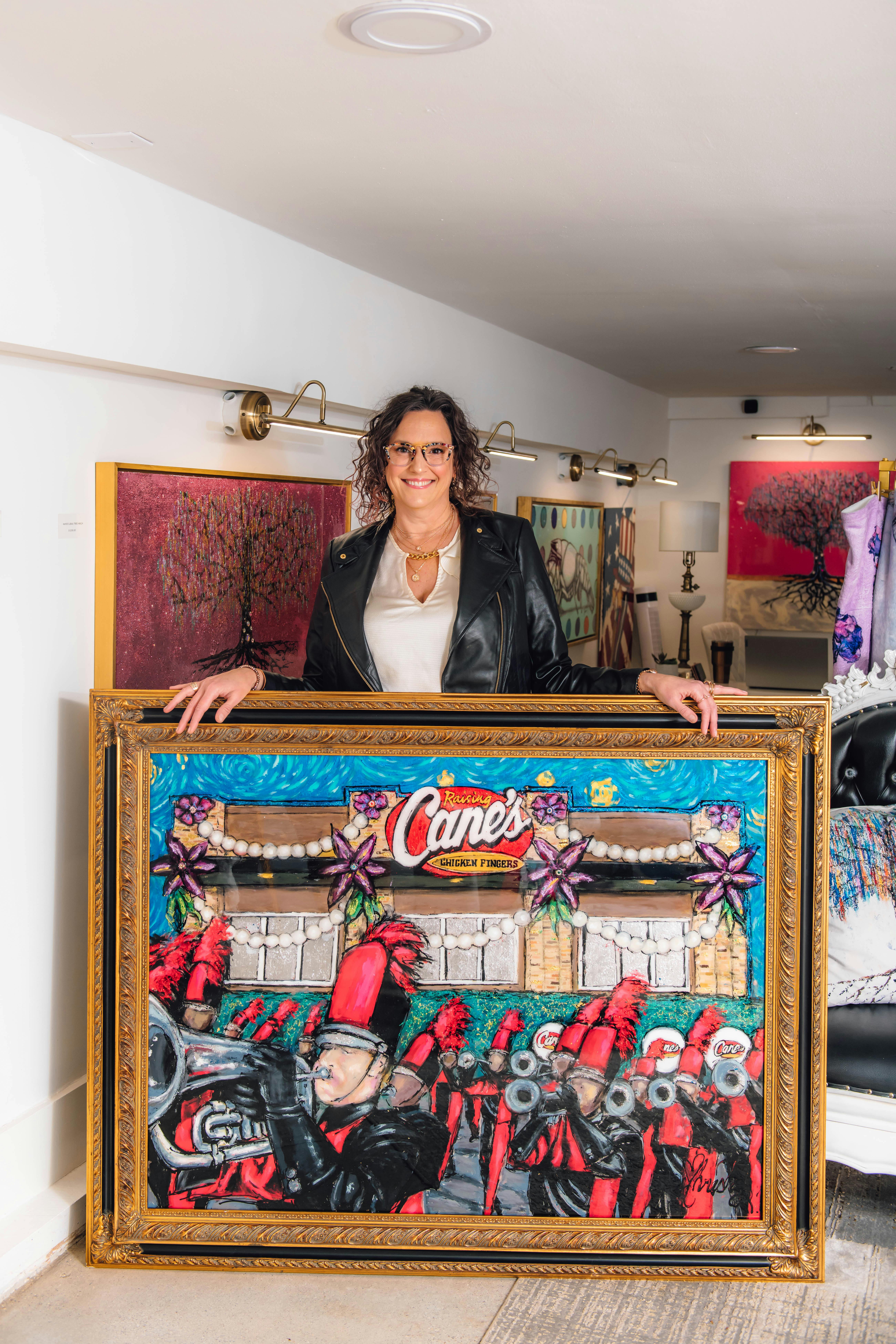 Artist Christy Boutte standing with her painting of Raising Cane's Restaurant with a marching band in front.