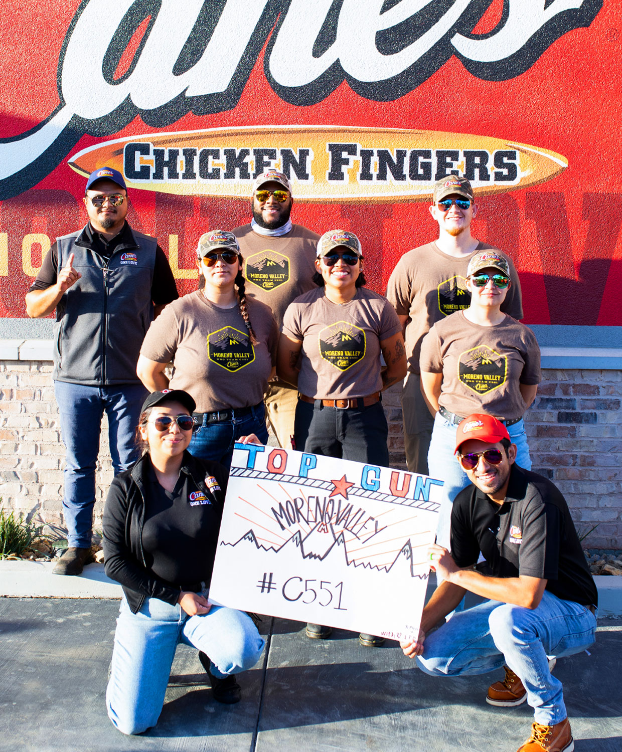 Crewmembers outside Raising Cane's holding a Top Gun sign