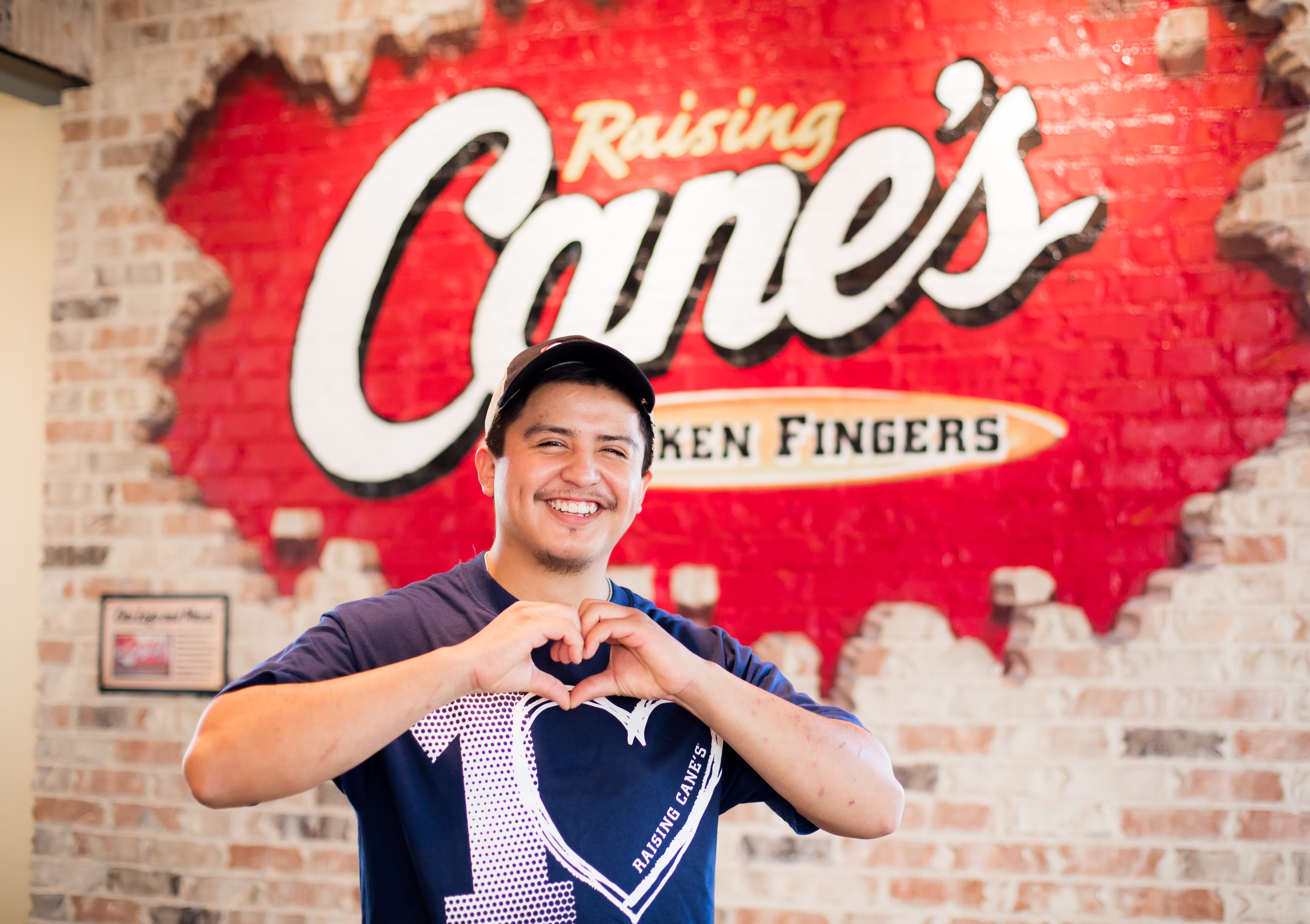 Raising Cane's Crew member in front of mural