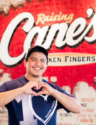 Raising Cane's Crew member in front of mural