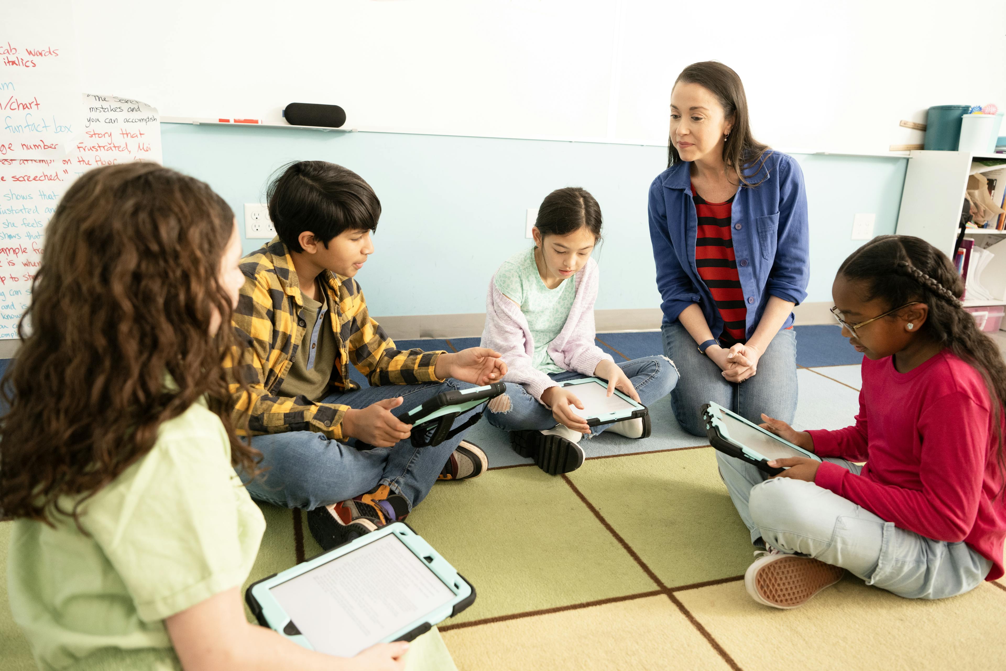 A teacher sits with a class of students on the floor