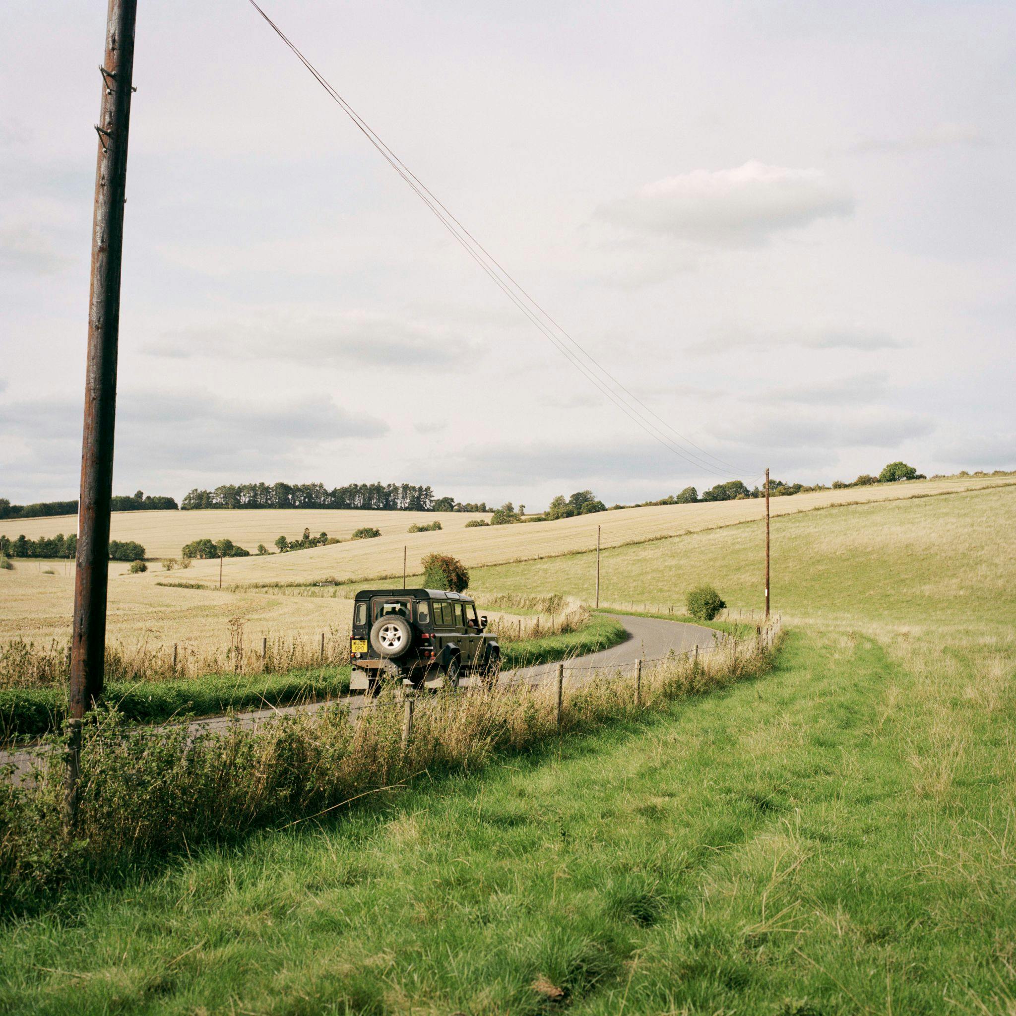 Green off-road car driving on a road between Ramsbury fields.