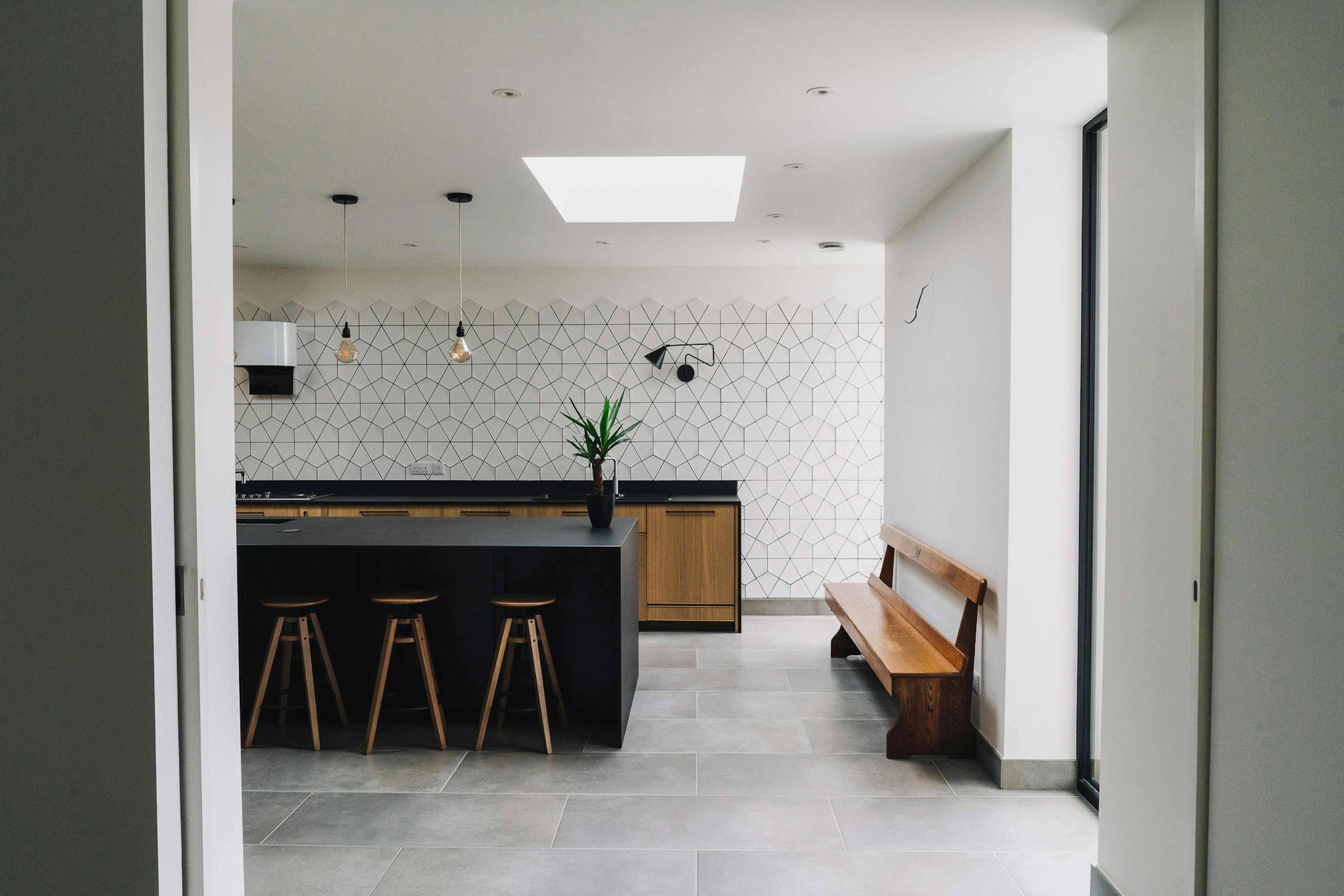 A view into the kitchen at Hillside, featuring a breakfast bar, black modern countertops and a bench. The room has a skylight.