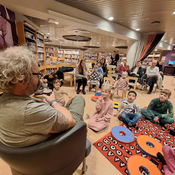 Maður situr í stól og talar við börn sem sitja á gólfi