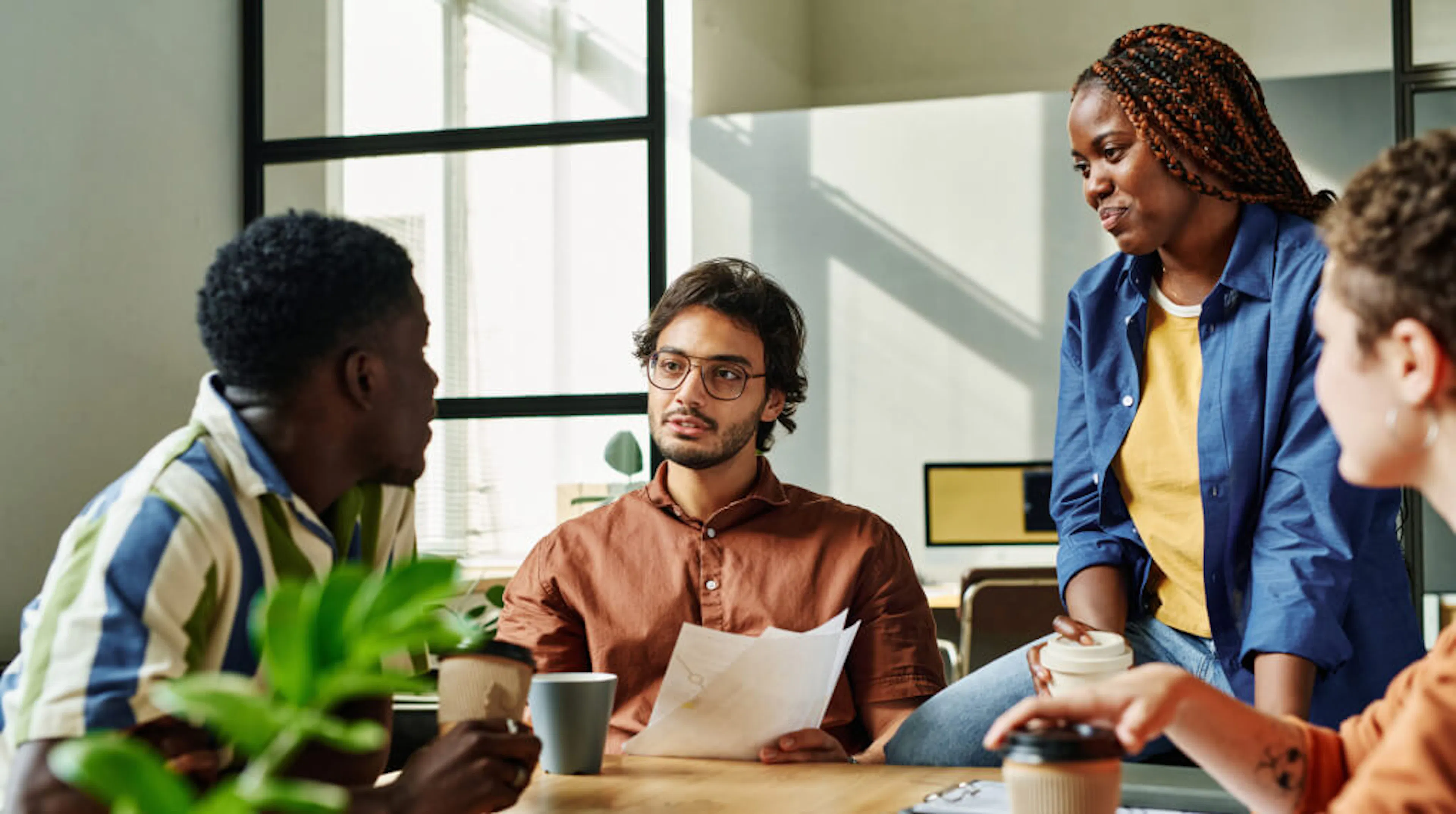 A team of employees discuss work in a meeting room with cups of coffee.
