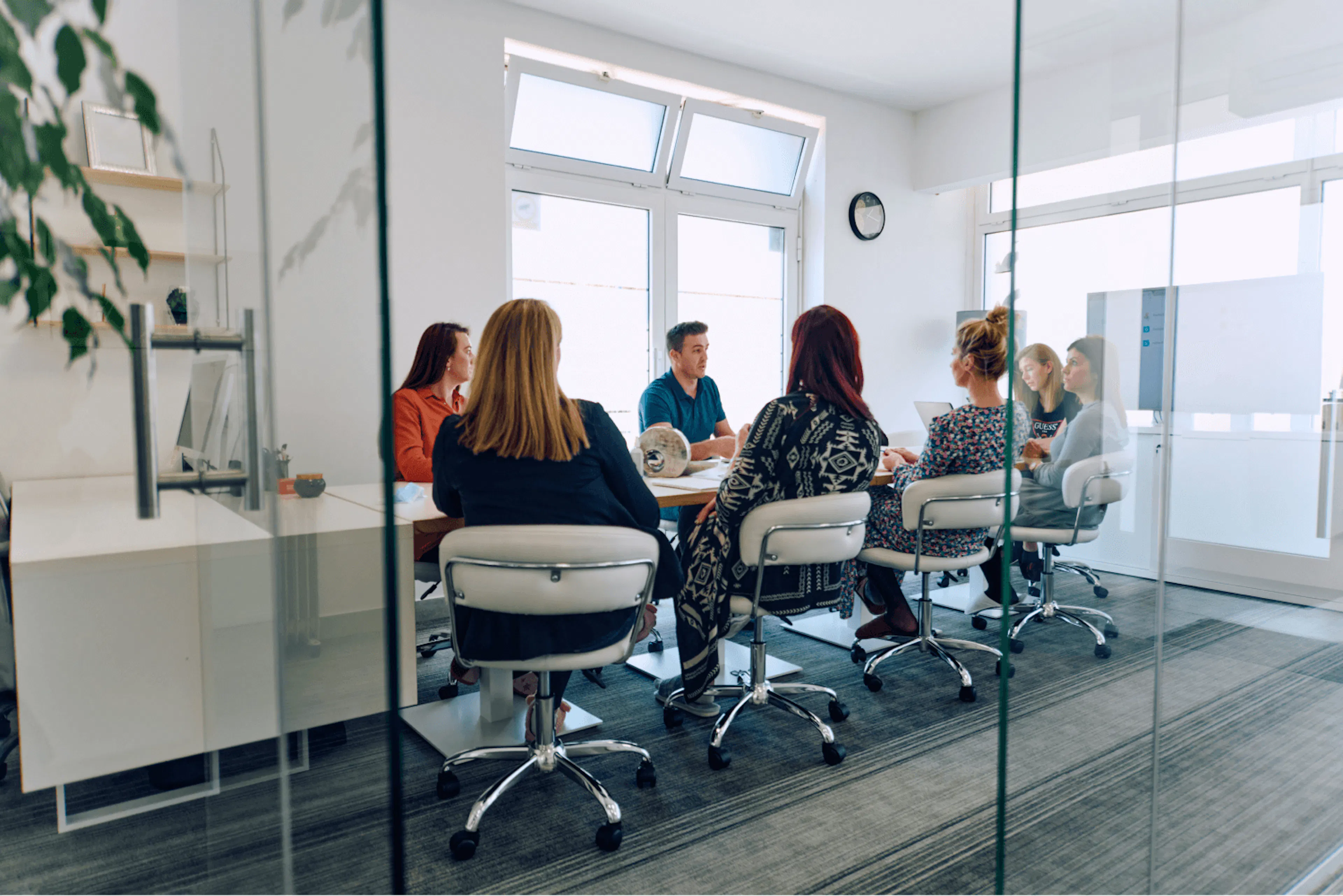 Photo showing a calibration meeting taking place. A group of managers sits around a meeting table, in a meeting room with glass windows.