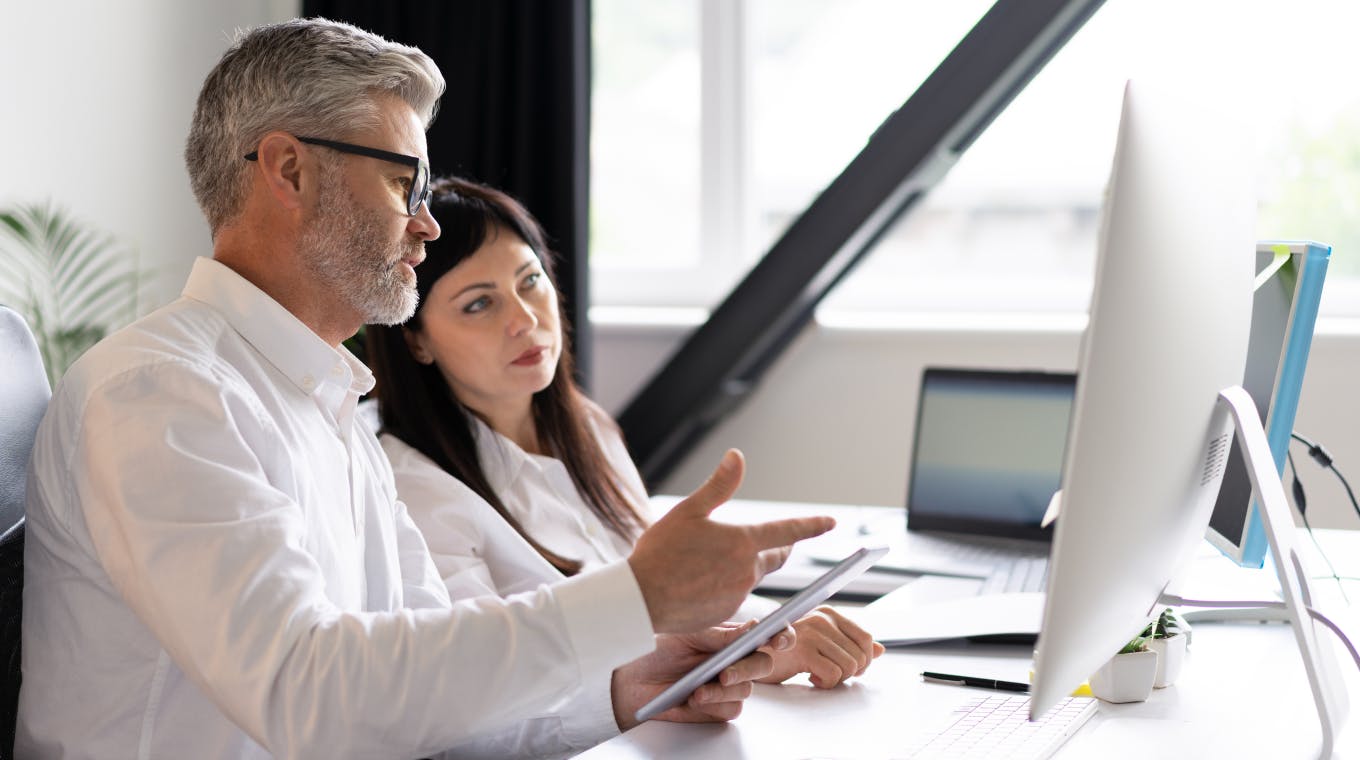 Two colleagues sit in front of a screen, discussing work.