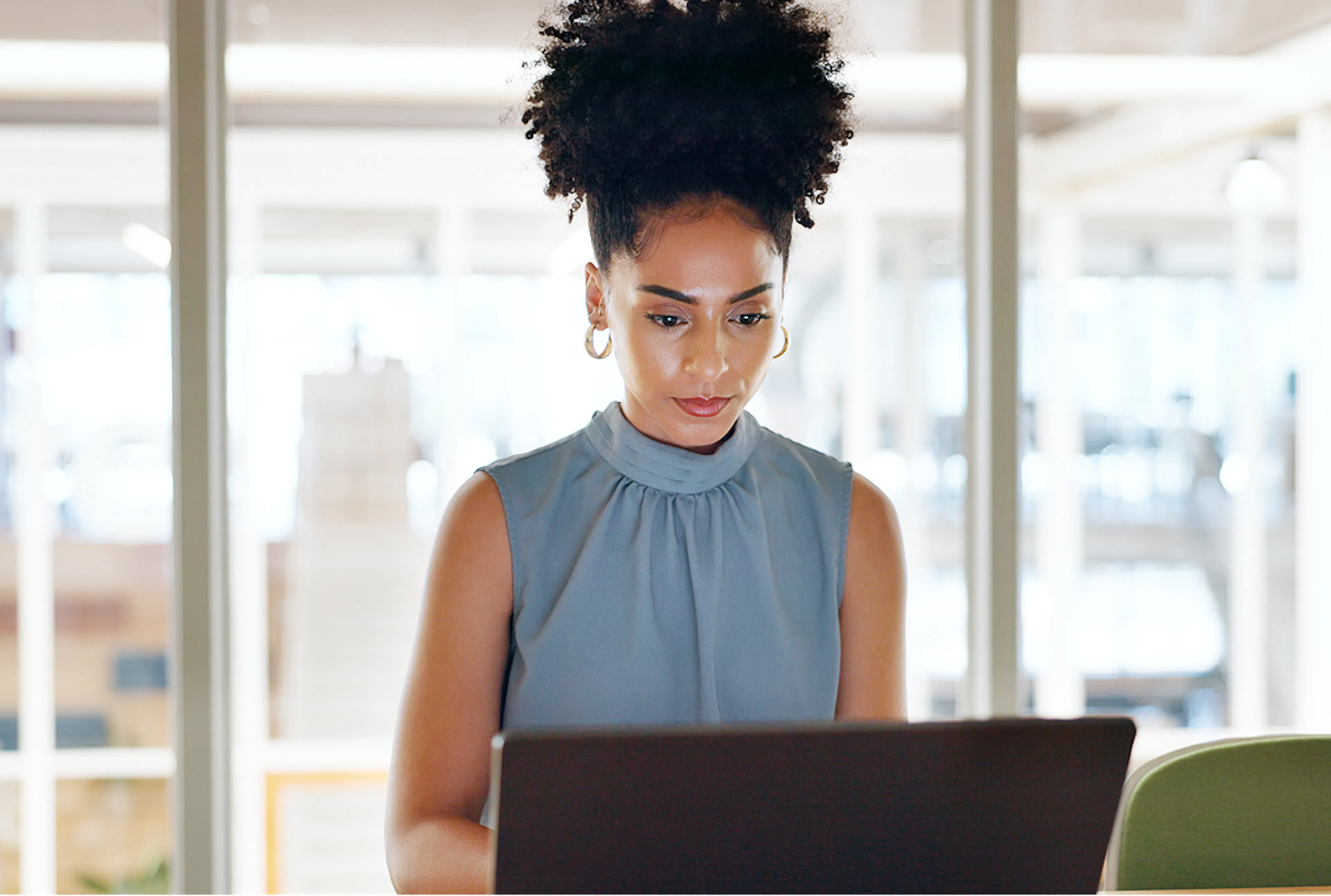 Businesswoman faces us, working on her laptop, in an office environment.