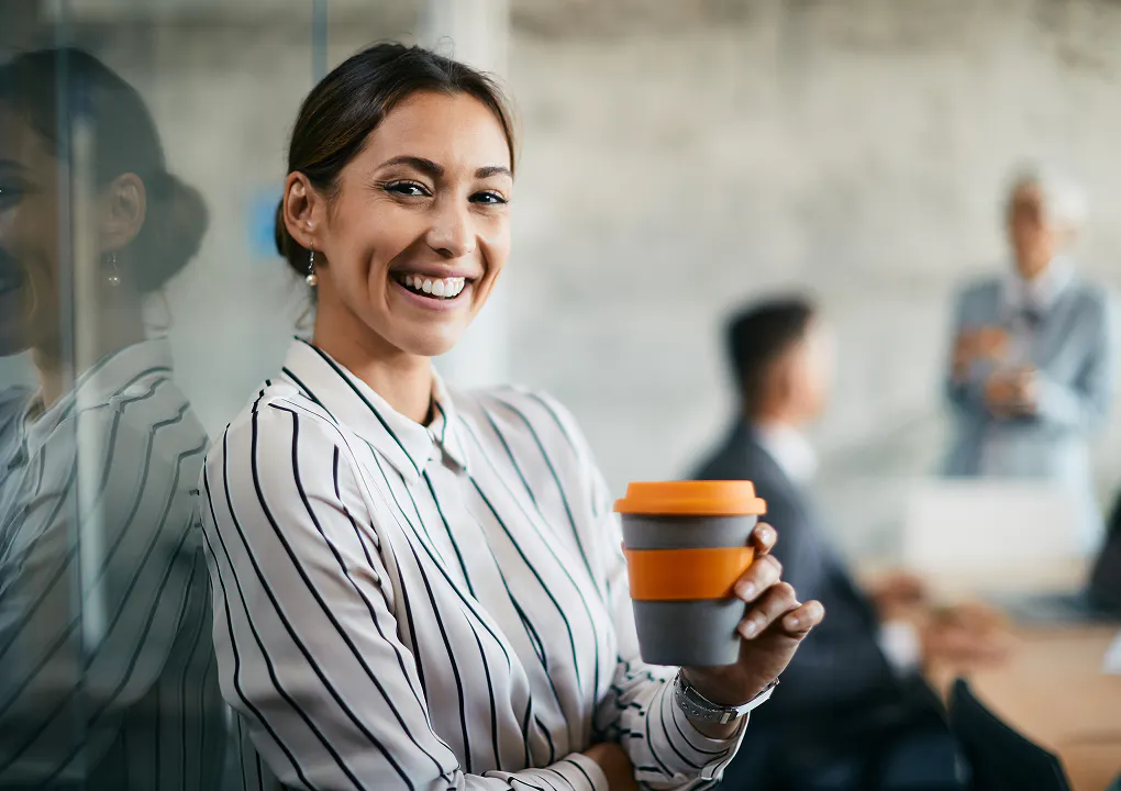 A young happy businesswoman holds a cup of coffee in an office environment