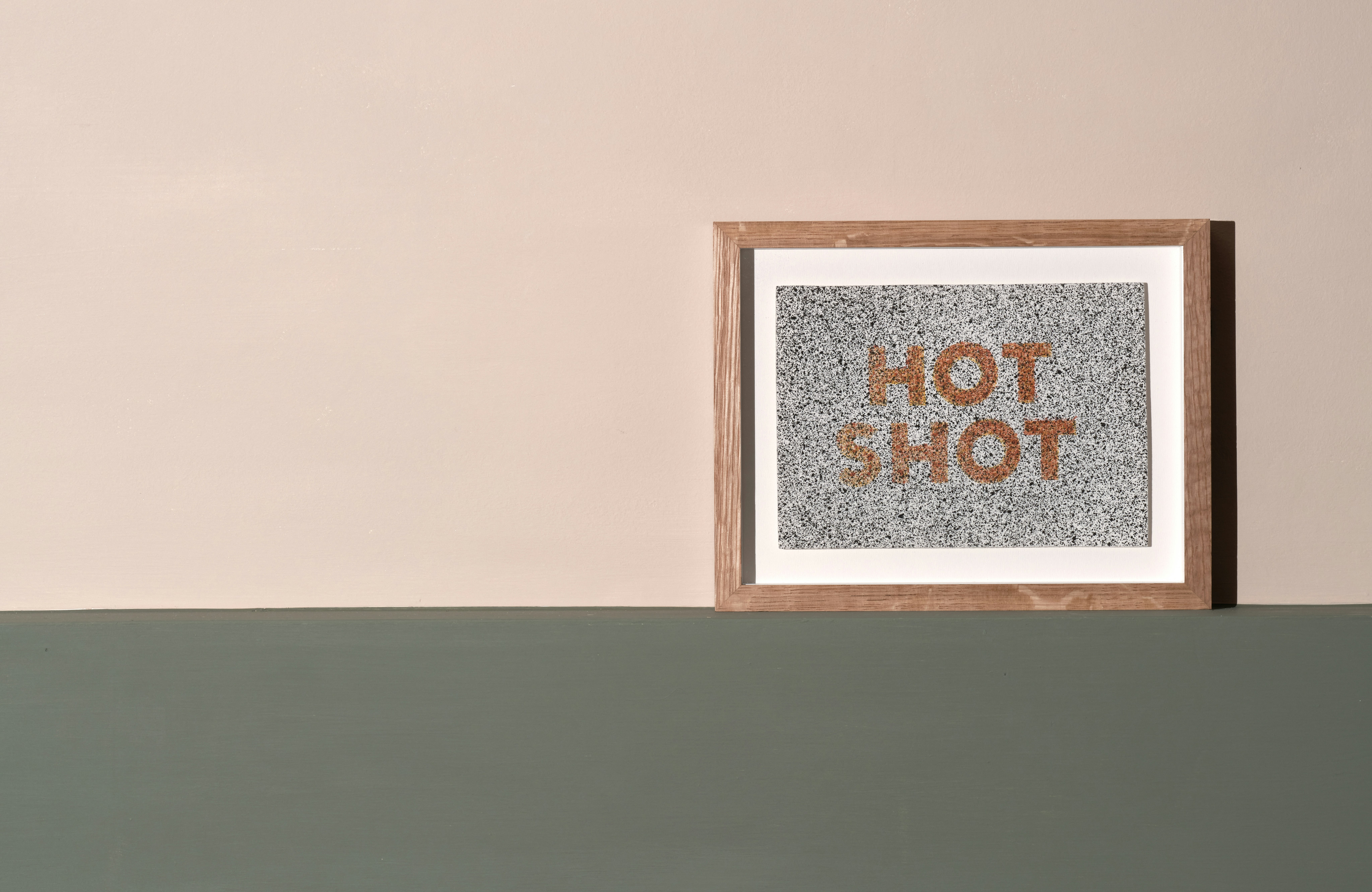 installation photograph of framed lithograph by Ed Ruscha with phrase hot shot in orange on white background and splashes of black all over