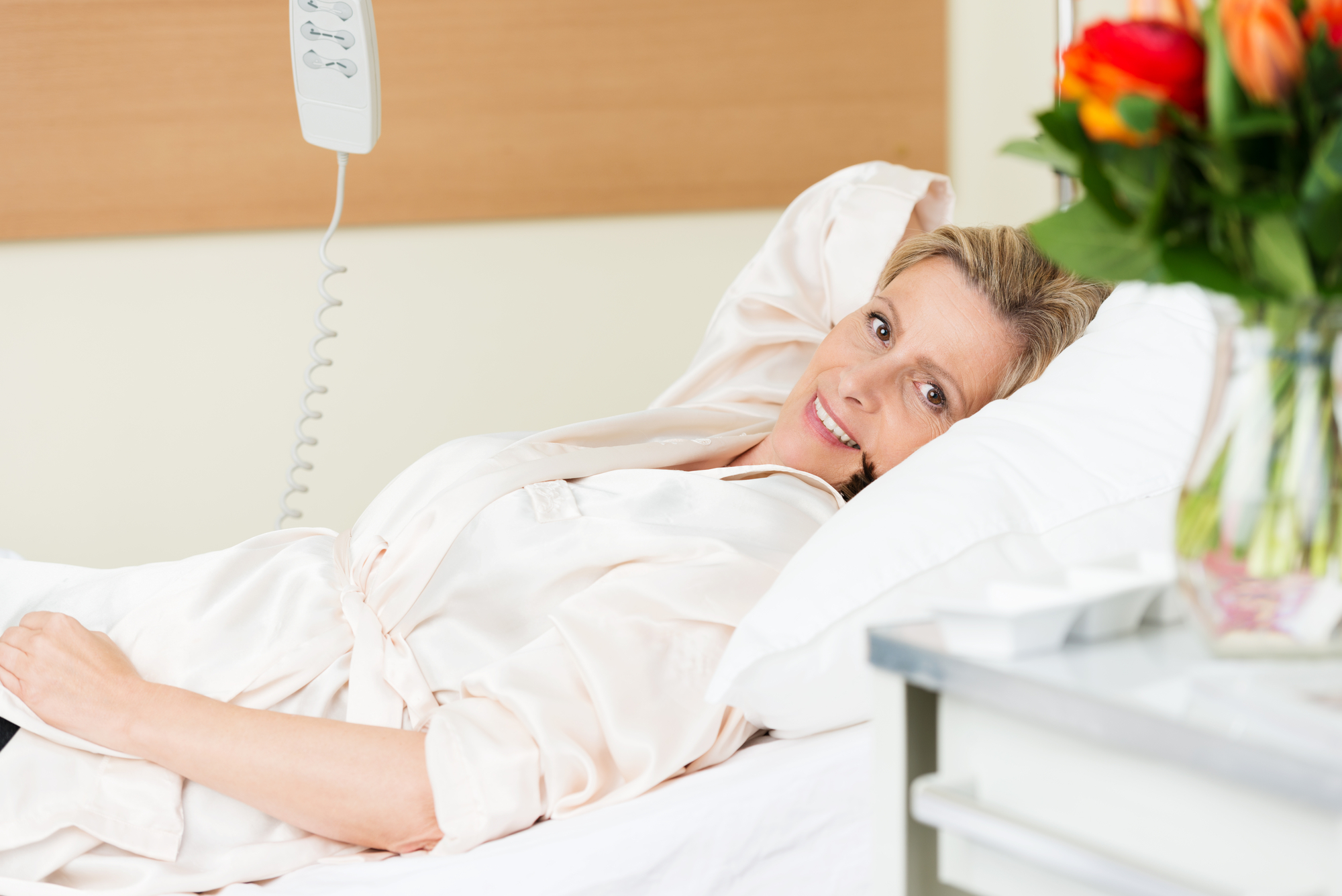 Vrouw in ziekenhuisbed met boeket op tafel naast bed