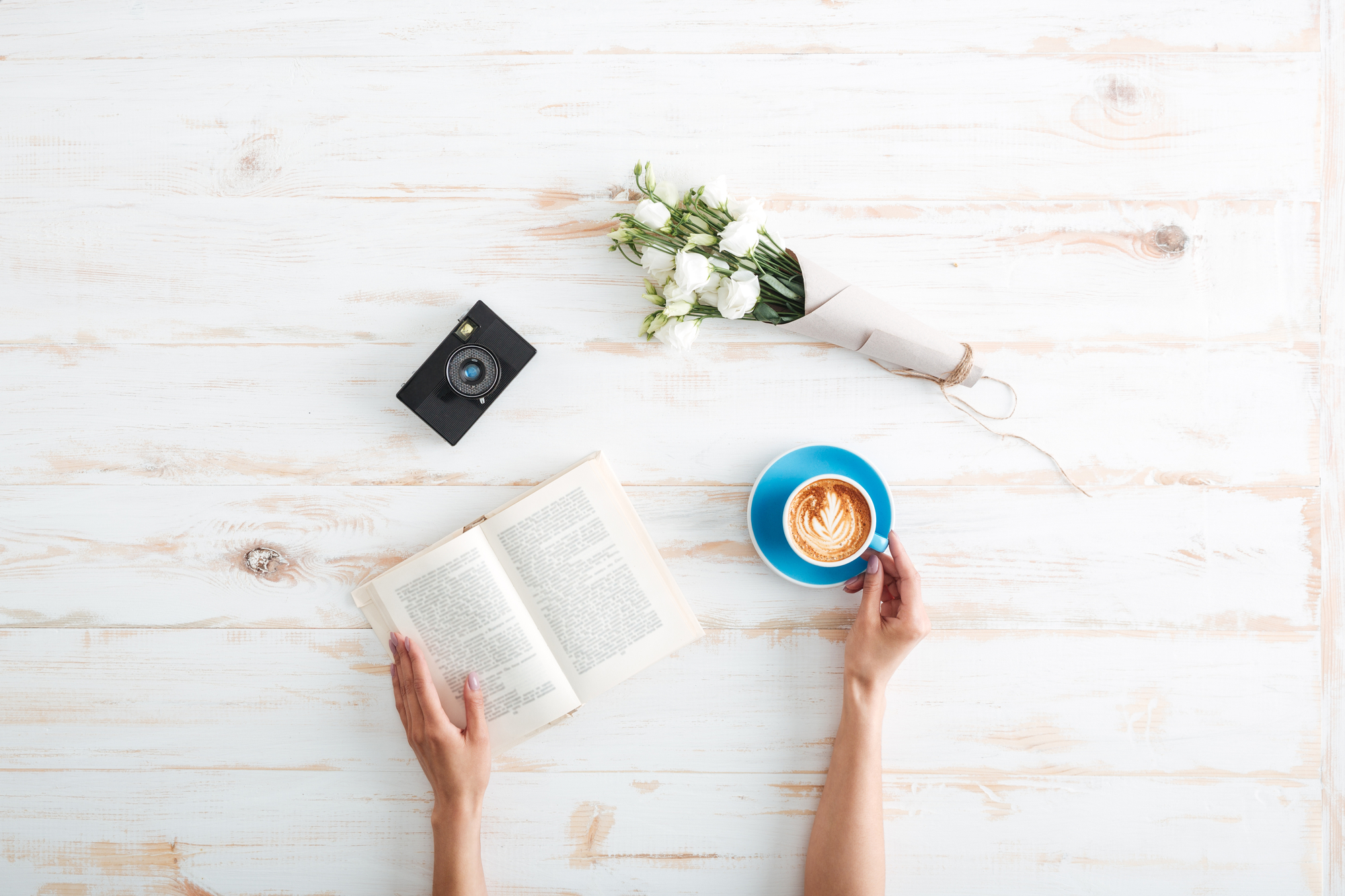 Een houten tafel met mobiele telefoon, boek, klein boeket en kop koffie