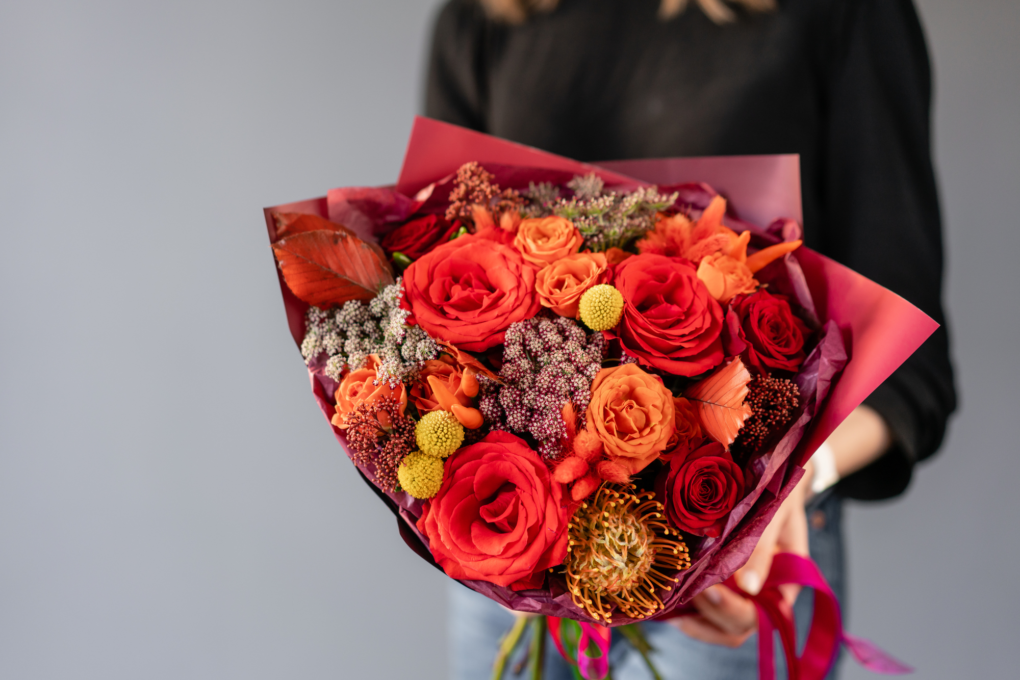 Vrouw in zwarte trui houdt boeket in rode kleuren vast