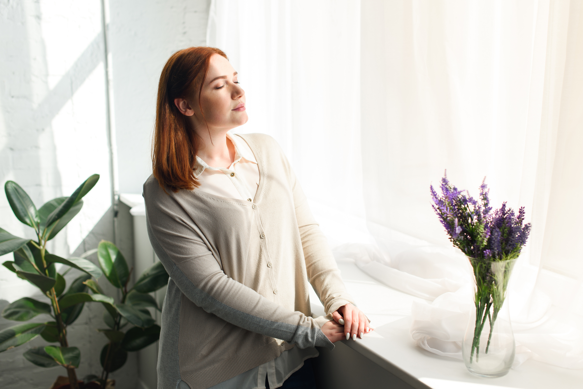 Een vrouw die voor het raam staat met haar ogen dicht
