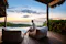 Person seated on a cushioned outdoor chair beside a private pool, overlooking the ocean at sunrise from a tropical beachfront villa.