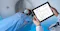 The image shows a patient undergoing a CT scan, with a medical professional holding a tablet displaying a dose report. The report includes details such as the scan type, CT dose, and total exam dose. The setting suggests a focus on monitoring and managing radiation exposure during medical imaging.