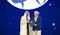 The image depicts two individuals on a stage, one wearing traditional Middle Eastern attire and the other in a suit, holding a certificate or award together. The background features a large globe graphic, suggesting an international or global event, possibly an awards ceremony or conference.