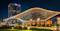 The image depicts a modern architectural structure illuminated at night, featuring the Hilton hotel in Uzbekistan. The building showcases a unique design with intricate patterns and is surrounded by landscaped greenery and lighting, creating an inviting and sophisticated atmosphere.