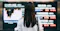 A woman intently observes a stock market board displaying various financial data and stock prices.