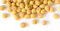 A close-up image of several yellow soybeans scattered on a white surface. The soybeans are round and smooth, with some showing a brown oval marking. The background is plain and bright, highlighting the color and texture of the soybeans.