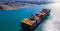 The image depicts a major shipping port with a large container vessel carrying multicolored containers. The port is bustling with activity, including cranes, docked ships, and extensive storage areas, highlighting global trade and logistics operations.