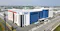 The image shows a large, modern industrial building labeled "Inari" and "P34," situated in a well-developed industrial area with multiple similar facilities nearby. The building's design and surroundings suggest it is part of a high-tech manufacturing or semiconductor production complex, highlighting advanced industrial infrastructure and corporate presence in the region.