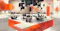 The image depicts a modern, abstract office environment with people working at desks surrounded by large, floating geometric cubes in shades of orange and black. The setting blends natural elements, such as autumn-colored trees, with a futuristic architectural design, suggesting themes of innovation, digital transformation, and the evolving nature of workspaces.
