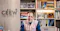 A person sits at a desk in front of a wall with the CEEW logo, surrounded by shelves filled with books, framed photos, and awards.