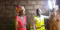 Two individuals stand inside a stone-walled room, one wearing a reflective vest and holding a bright LED light mounted on the wall.
