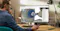 This image shows a person working at a desk, using a computer with Autodesk software open on the screen. The software displays a 3D model of a mechanical part, likely related to engineering or design. The workspace includes a keyboard, mouse, lamp, and some stationery, creating a professional and focused environment suitable for CAD (computer-aided design) work.
