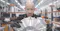 This image shows a person wearing black gloves and holding a large metallic component, possibly a motor or part of an industrial machine, in a modern manufacturing or engineering facility. The background features shelves, computer workstations, and industrial lighting, indicating a high-tech workspace focused on advanced engineering or production. The individual appears to be inspecting or presenting the component, suggesting a context of quality control, assembly, or demonstration.