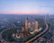 Aerial dusk view of Istanbul Financial Center, with illuminated modern skyscrapers clustered in the foreground, highways curving around the complex, and the city stretching to the horizon under a pink and blue evening sky.