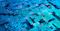 Abstract close-up of a glowing blue digital circuit board overlaid with streams of binary-style numbers and data, representing computing, AI, or cybersecurity.