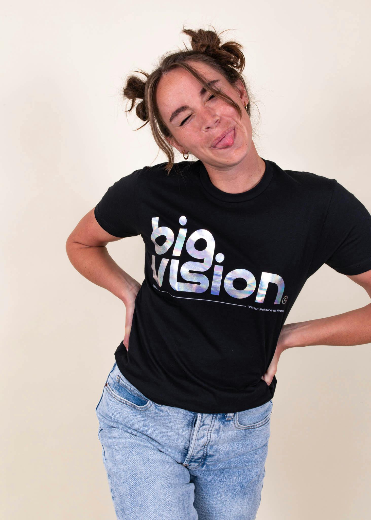 A girl sticks her tongue out playfully while wearing a shirt that says "big vision" printed with metallic foil
