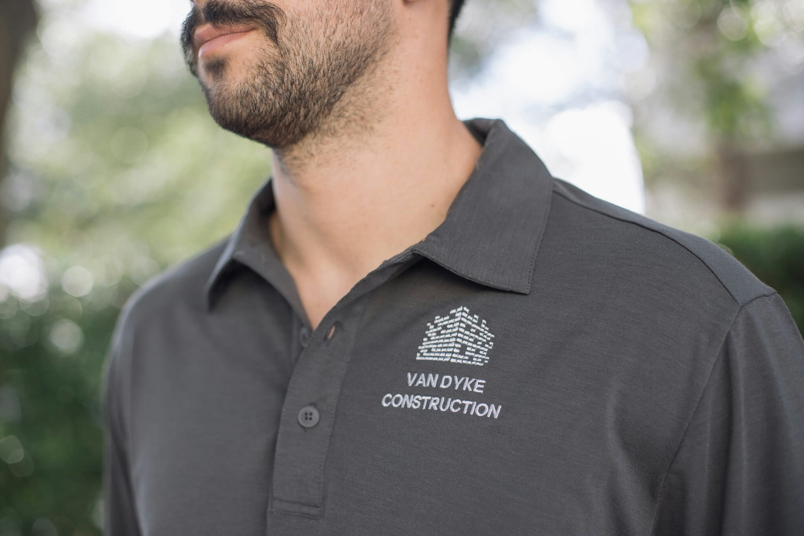 A man with a mustache wears a polo with a construction company's logo embroidered on it 