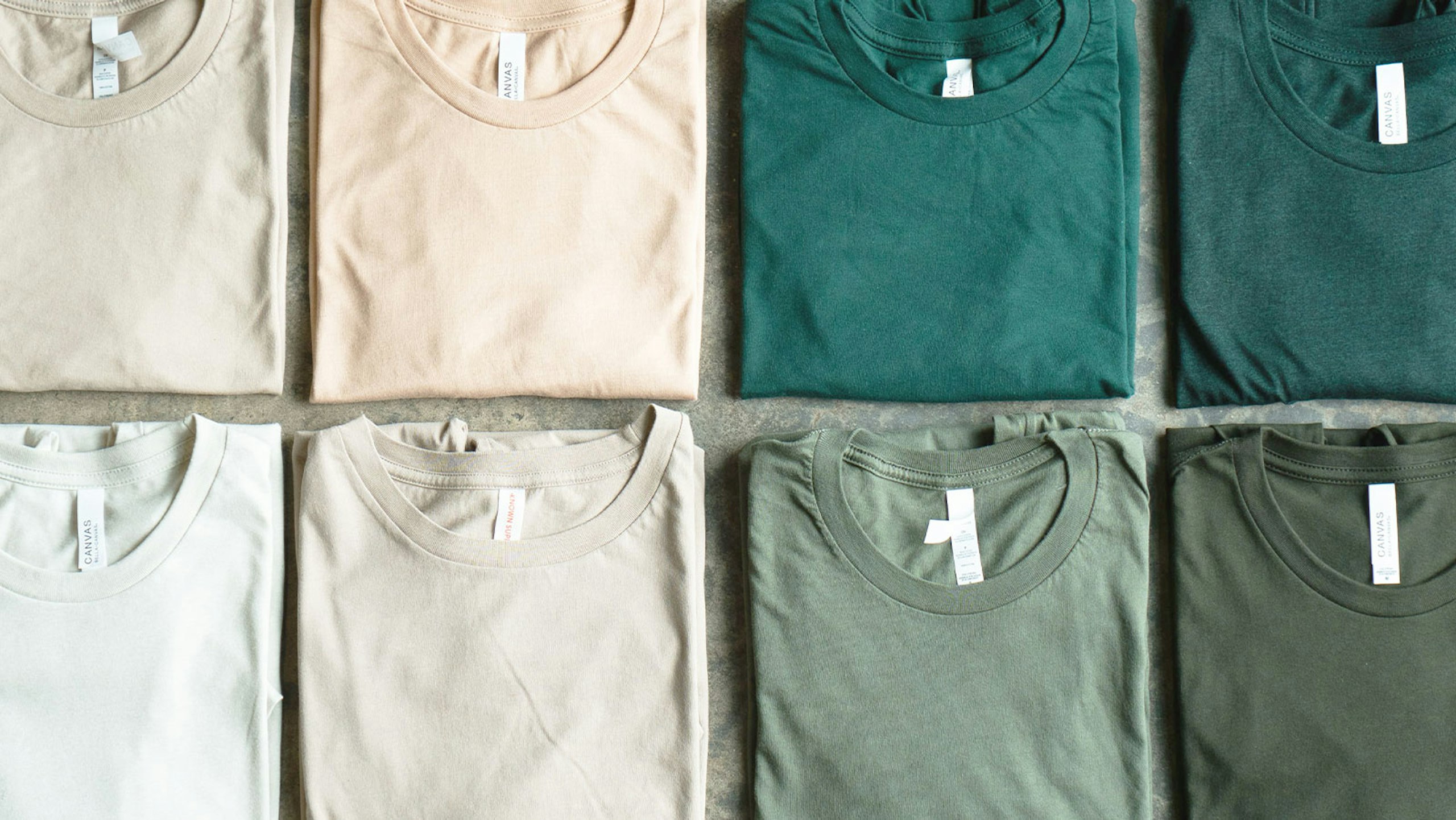 8 t-shirts, folded, and each one ranges from neutral to green in color.