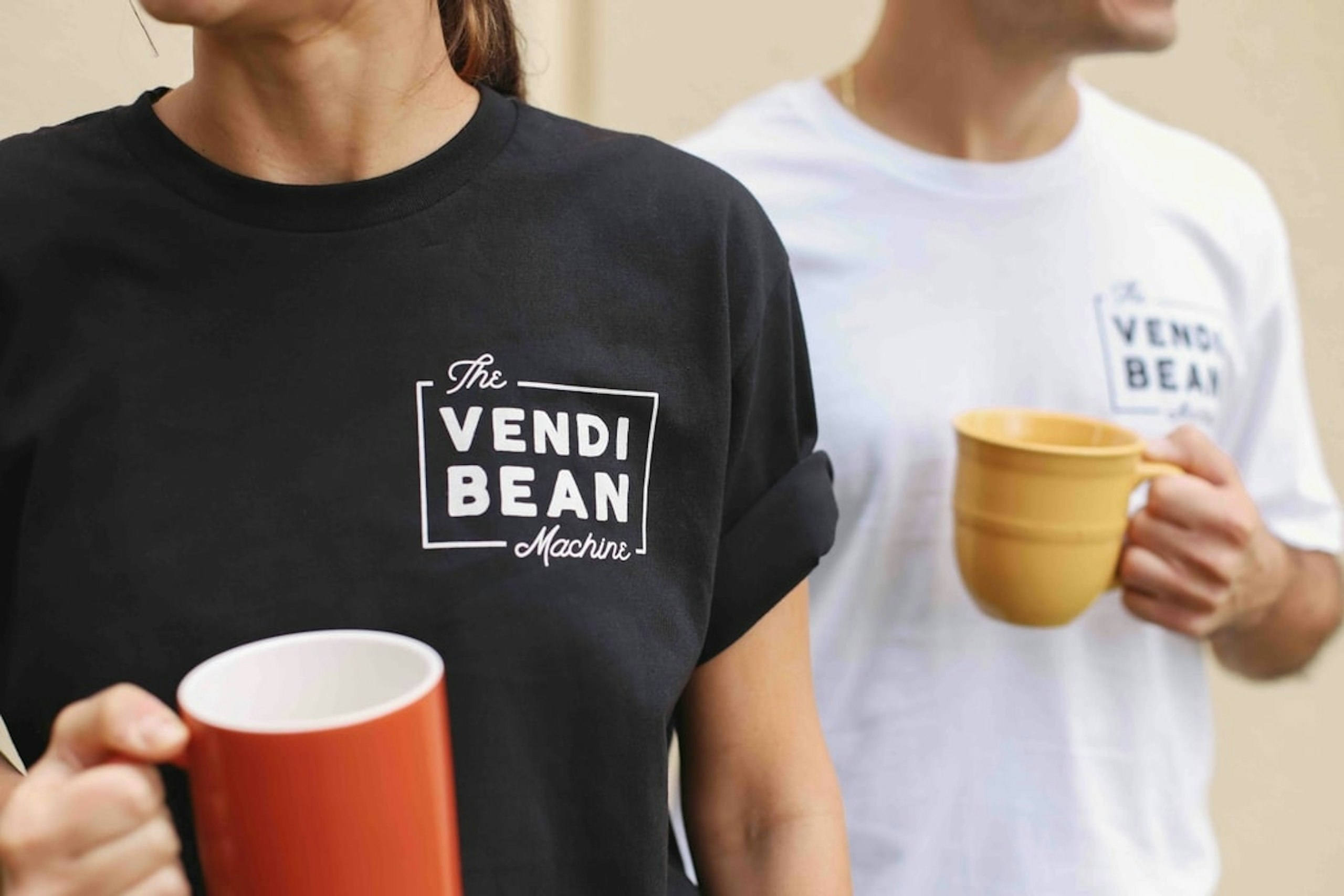 Two people wear shirts for a coffee shop, one in black with white text, the other white with black text.