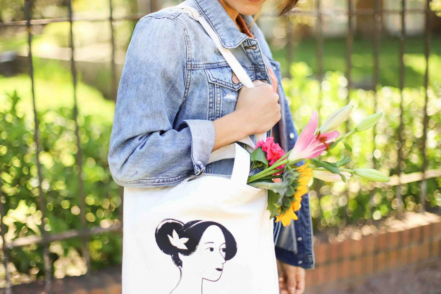 person holding a white tote with flowers coming out of it