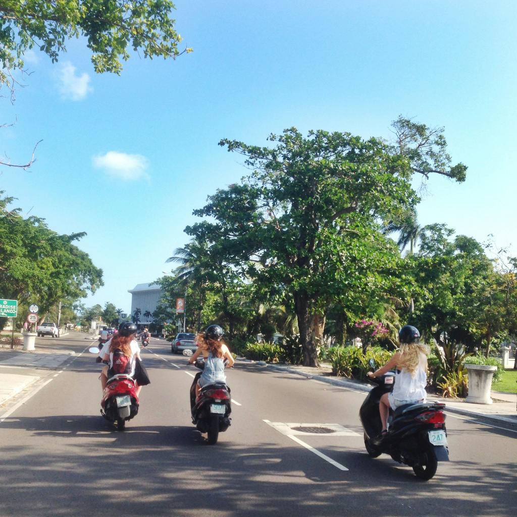 three people riding scooters down the street