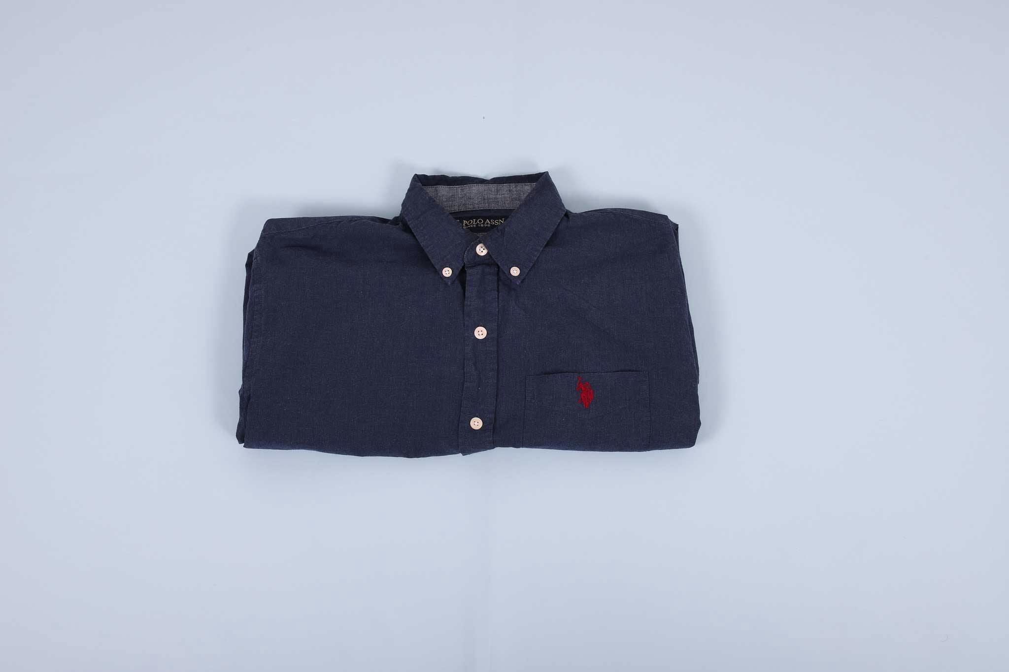 Navy buttoned up shirt folded into thirds agains a light blue background Navy buttoned up shirt folded into thirds agains a light blue background