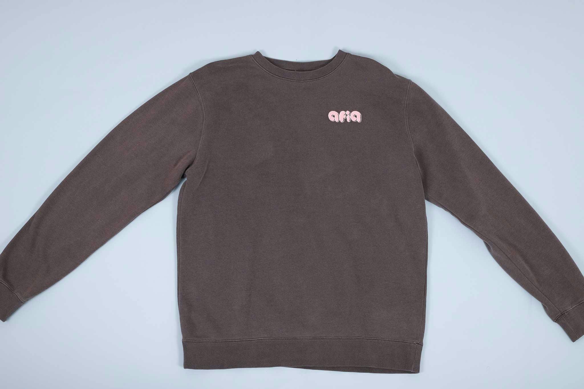 Grey sweater with pink text on the chest spread out on a light blue background Grey sweater with pink text on the chest spread out on a light blue background