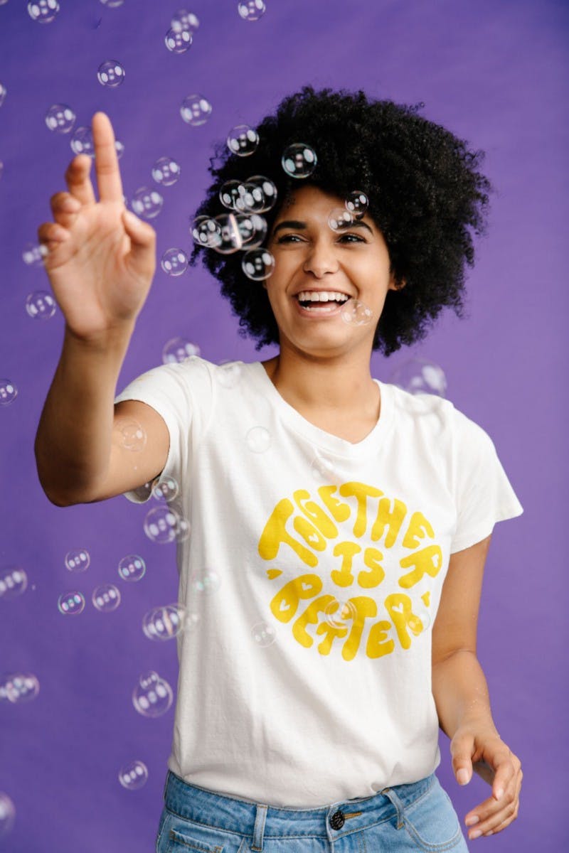 women wearing a white shirt with yellow print in front of a purple background women wearing a white shirt with yellow print in front of a purple background