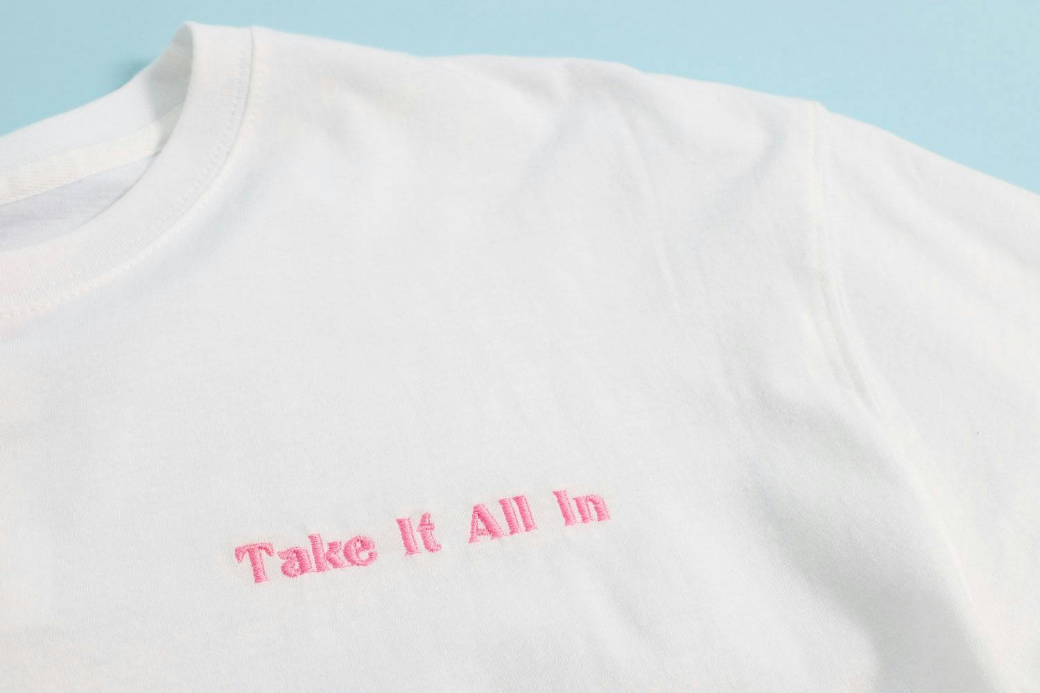 white shirt with "take it all in" embroidered in pink text white shirt with "take it all in" embroidered in pink text